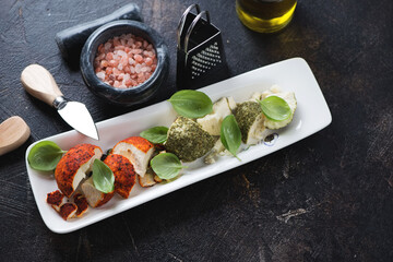 White plate with swiss belper knolle cheese, green basil leaves and pink salt, elevated view on a dark brown stone background