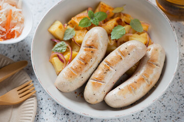 Close-up of fried german traditional white sausages served with potato salad, horizontal shot on a beige granite background