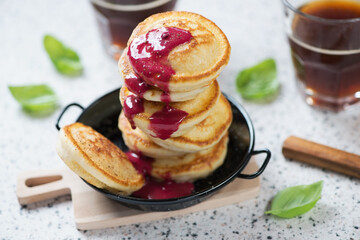 Black serving pan with mini pancakes, studio shot on a beige granite surface with glasses of black coffee in the background