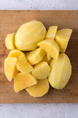 chopped and whole peeled raw potatoes on a wooden board surface, closeup view taken from above