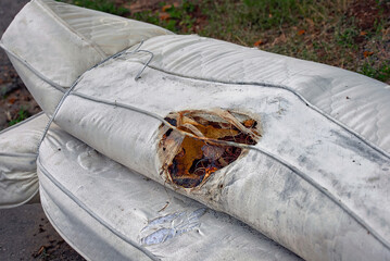 Damaged mattress with fire burnt hole thrown out as junk. Burning stains from being burnt. Fire...