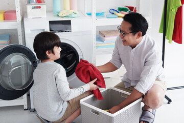 Smiling Asian father and little boy child are putting the clothes in the washing machine and Washing together in Laundry room on holiday.They are Family activities and child educational for home
