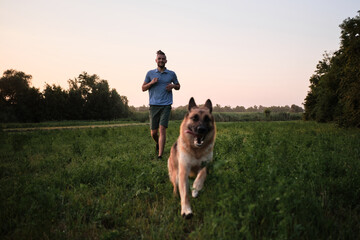 Young handsome Caucasian man with beard and dreadlocks is walking with dog on warm summer evening...