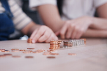 Fototapeta premium Smiling Asian little asian girl child is counting coins on wwoden table for saving money for the future with mother on wooden table. Child educational for homeschool concept.