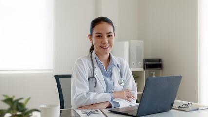 Fototapeta na wymiar Young adult asia people or medic staff woman sitting toothy smile arm cross look at camera happy work on desk in clinic office room in telehealth telemedicine smart health care consult online service.