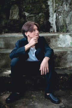 A young teenage Filipino man in deep contemplation while sitting on concrete steps outside.
