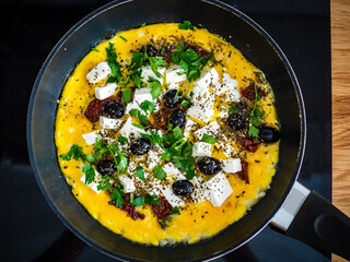 Delicious breakfast - scrambled eggs with feta cheese, sun-dried tomatoes and black olives served in frying pan
