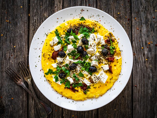 Delicious breakfast - scrambled eggs with feta cheese, sun-dried tomatoes and black olives served on wooden table
