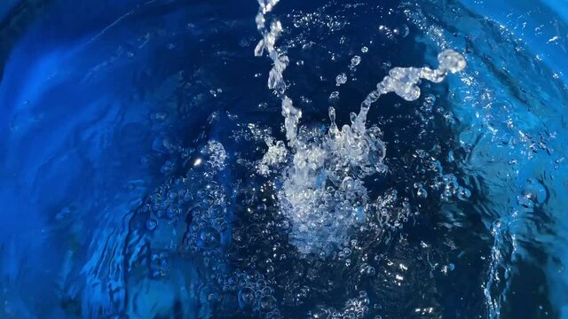 A jet of clean water pours into a blue barrel, splashes fly away