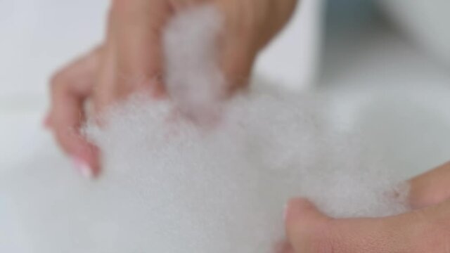 Close-up. The girl touches the white voluminous artificial fluff and sometimes breaks it