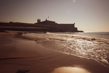 sunset at Carcavelos beach and the silhouette of Sao Juliao da Barra fort - sea defensive...
