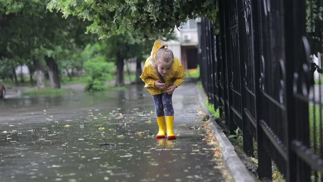 Excited child runs in the rain in a yellow raincoat