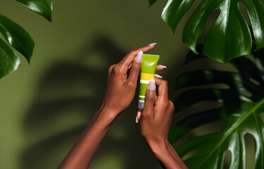 Natural skin care concept. Photo of females hands holding a cream against green tropical plants