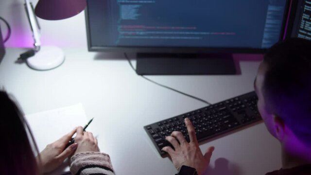 Two colleagues programmers are sitting in front of a monitor and typing coding language. Man and woman are discussing their work. Concept of making websites and software. Freelance in cyberspace theme