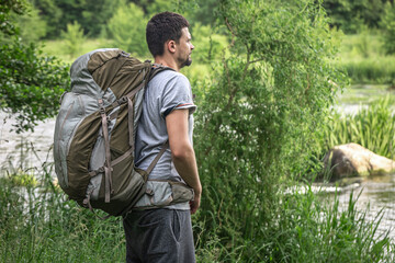 Male traveler with a large hiking backpack near the river.