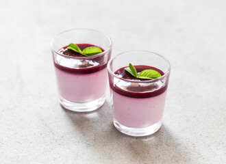 Italian dessert Panna Cotta black currant with berry sauce in a glass on a light background