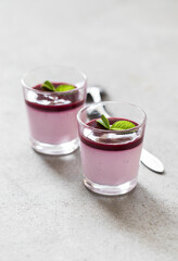 Creamy berry dessert, Panna Cotta black currant with sauce in a glass on a light background