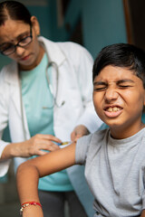 Young Indian boy receiving an injection by female doctors and shouting.  