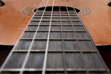 Close-up of old acoustic guitar fretboard with selective focus in the center. Neck perspective with blurred soundhole and strings. Music concept