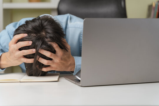 Stressed Young Businessman, Trader Or Investor Touch Head, Disappointed When Bad Investment Or Economic Crisis, Losing Money From Investing, Trading Stock, Cryptocurrency As Bitcoin On Laptop At Home.