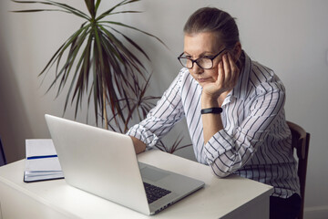 woman in a white striped shirt aged sits at a computer at home with glasses