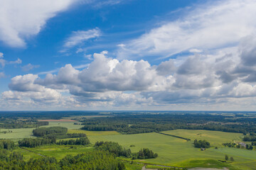 Aerial view of green forests surrounded by green farmland fields. Blue sky with white clouds