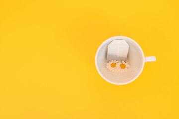 A tea bag with chamomiles in a cup on a yellow background. The spring-summer concept. Top view, place to copy
