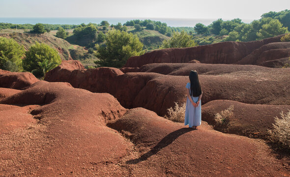 rear view of girl in blue dress standing in red crater in Puglia, Italy in Cava di Bauxite near Otranto