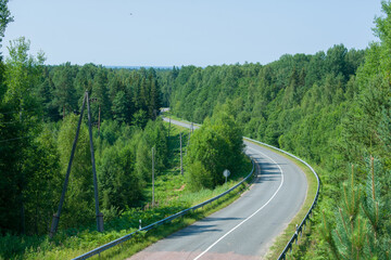 Fototapeta na wymiar Empty winding asphalt road going through green forest