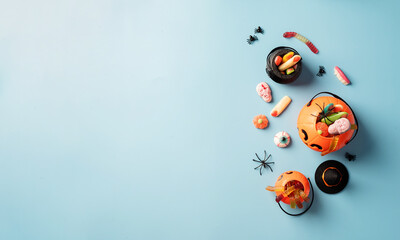 Various halloween sweets and candies in a pumpkin pot top view on blue solid background with copy...