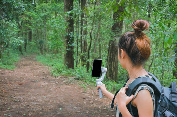 Young women using smart phone and gimbal when her trekking in forest , inspiration , motivation and camping activity concept