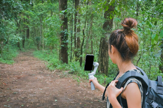 Young women using smart phone and gimbal when her trekking in forest , inspiration , motivation and camping activity concept
