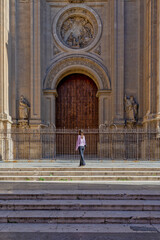 Young girl with purple sweater from behind looking at the closed main door of the cathedral of Granada