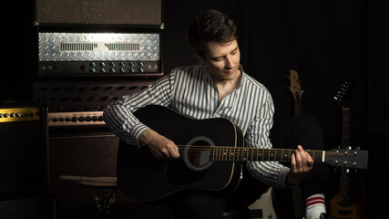Obraz premium Handsome young acoustic guitar blues player performing his musical skills. Hipster Guitar player strumming. Handsome young male musician playing guitar in recording studio.