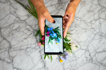 Anonymous florist taking photo of flowers in studio