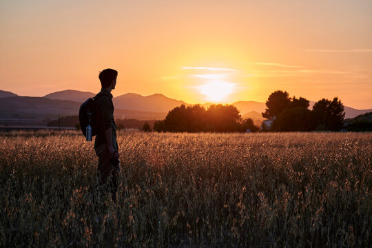 Silhouette of a photographer looks at the sun in a meadow at sunset