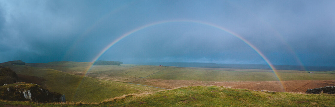 A double rainbow fills a dark blue sky along Hadrian's Wall in the UK.