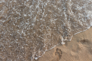 Foamy ocean water washes away footprints on sandy beach