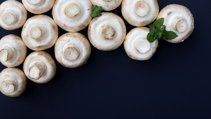 Fototapeta na wymiar Champignon mushrooms and mint leaves on a dark background