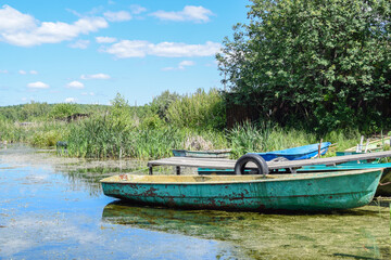 Naklejka na ściany i meble Old fishing boats near the pier in the lake or river. Summer sunny day. Abandoned boat. Boat dock.