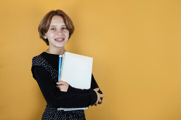 Teen girl with books and notebooks on a yellow background, place for text. The girl happily goes to high school. The concept of back to school