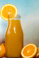 Fresh orange juice with orange slice in bottle glass on moody blue textured background