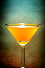 Martini glass with a mix of orange juice and alcohol against dark and moody orange blue background