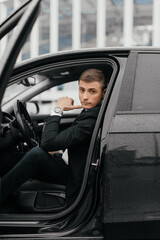 a handsome young man in a black suit is sitting in a car