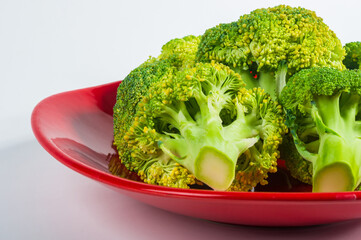 Sliced raw fresh head of broccoli cabbage in a red plate on white background, healthy vegetarian food, close-up