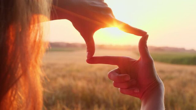 Woman makes a frame with her hands on a sunset background. Business planning and strategy concept.