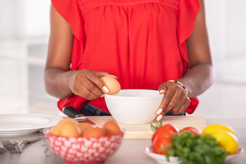 Close up of afro american woman holding an egg to the edge of a bowl