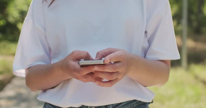 A woman in a white T-shirt prints a message on her smartphone, hides the phone screen to her body and stops the camera in front of her with her hand. Confidentiality of a person's personal life.