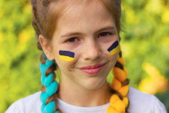 smiling Ukrainian girl with blue and yellow flags painted on her cheeks. patriotism concept, flag day and independence day of Ukraine. sports and support of fans.