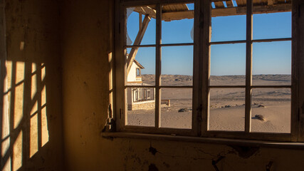 View of the desert and a house through on of the neglected window frames of a house at the ghost town of Kolmanskop, Namibia